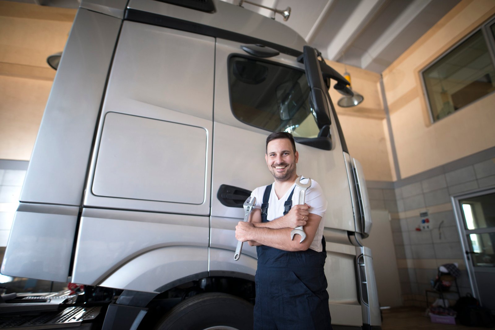 Professional vehicle mechanic standing in workshop with crossed arms and wrench tool ready to start repairing truck.